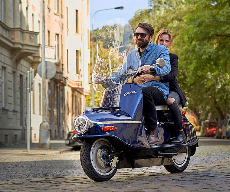 Čezeta Type 506 azul con dos personas a bordo recorriendo la ciudad